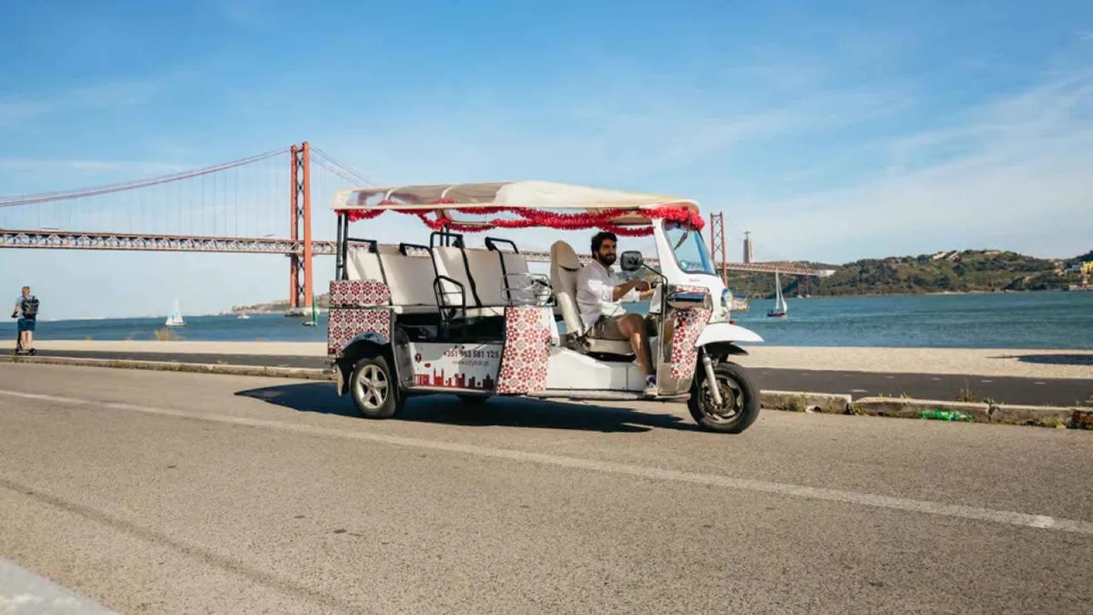 Private tuk-tuk climbing a cobbled Alfama street on a guided tuk-tuk tour with hotel pickup in Lisbon
