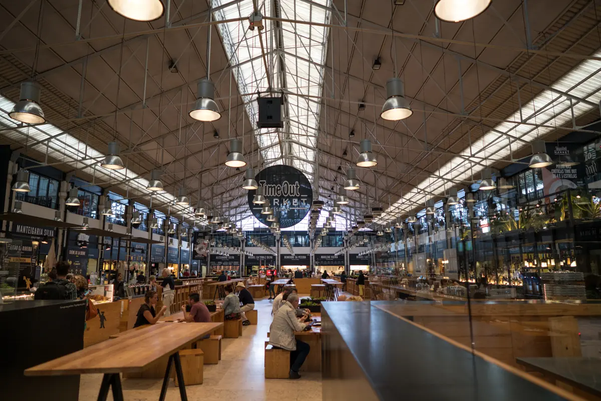 The main hall of the Time Out Market food hall, long shared tables under the iron roof of the Mercado da Ribeira